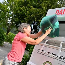 Eine Frau wirft eine Kleiderspende in einen Altkleidungscontainer