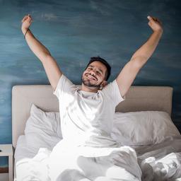 Ein Mann streckt sich in einem Bett.