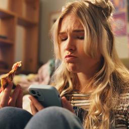 Eine junge Frau schaut traurig auf ihr Telefon