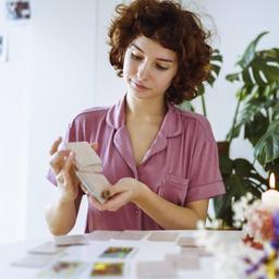 Junge rothaarige Frau sitzt zu Hause am Tisch und legt Karten für Wahrsagerei aus.