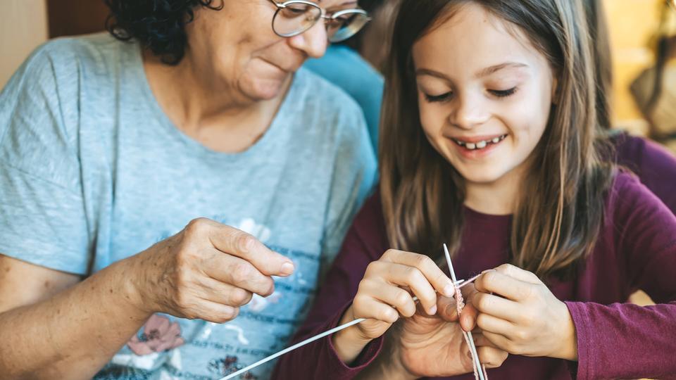 Eine Großmutter hilft ihrer Enkelin beim Stricken.