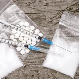 Pulver in Tütchen, Tabletten und Spritzen liegen auf einem Tisch.